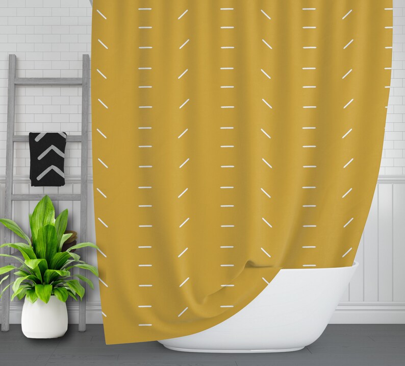 May include: A mustard yellow shower curtain with a white geometric pattern. The curtain is hanging in a bathroom and is partially covering a white bathtub.