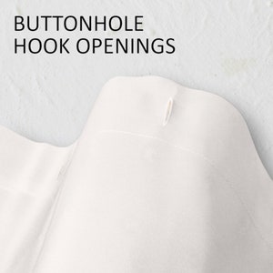May include: Close-up of white fabric with the text "BUTTONHOLE HOOK OPENINGS" at the top. The fabric has a buttonhole opening. The fabric is likely part of a garment or home textile.