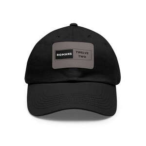 May include: Black baseball cap with a grey patch that says "Romans Twelve Two" in white text.