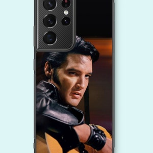 May include: A black phone case featuring a photograph of Elvis Presley wearing a black leather jacket, looking over his shoulder, holding a guitar. The phone case has a black camera bump with a carbon fibre texture.