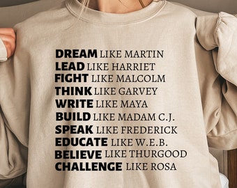 Könnte beinhalten: Beigefarbener Pullover mit schwarzem Text, der "DREAM LIKE MARTIN, LEAD LIKE HARRIET, FIGHT LIKE MALCOLM, THINK LIKE GARVEY, WRITE LIKE MAYA, BUILD LIKE MADAM C.J., SPEAK LIKE FREDERICK, EDUCATE LIKE W.E.B., BELIEVE LIKE THURGOOD, CHALLENGE LIKE ROSA" lautet.