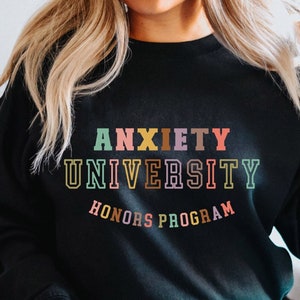 Könnte beinhalten: Schwarzer Pullover mit dem Text "Anxiety University Honors Program" in bunten Buchstaben.