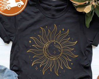May include: Black t-shirt featuring a gold sun and moon design. The sun has rays and the moon is crescent shaped. There are small stars around the sun and moon.