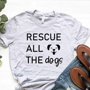 K&ouml;nnte beinhalten: Ein graues T-Shirt mit dem Text "RESCUE ALL THE dogs" und einer schwarzen Silhouette eines Hundes mit herausgestreckter Zunge.