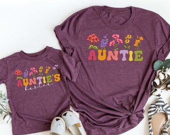 May include: Two purple t-shirts with a floral design and the text "Auntie" and "Auntie's Little" in rainbow letters.