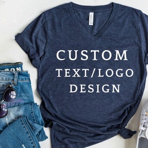 Peut inclure: Un t-shirt bleu marine à col en V avec le texte "CUSTOM TEXT/LOGO DESIGN" imprimé en blanc sur le devant.