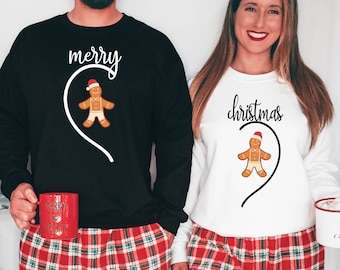 Może przedstawiać: Para w dopasowanych świątecznych piżamach z wzorem piernikowego ludzika. Koszulka mężczyzny głosi "merry", a koszulka kobiety "christmas".