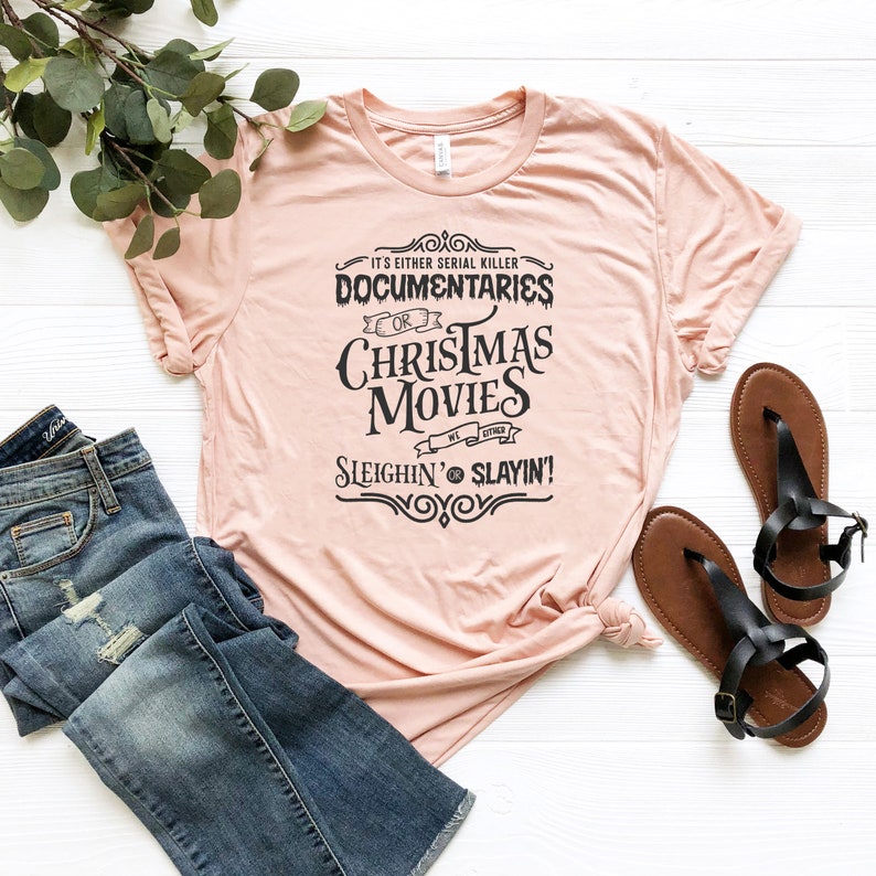 May include: A pink t-shirt with a black graphic that reads "It's either serial killer documentaries or Christmas movies we either sleighin' or slayin'!".