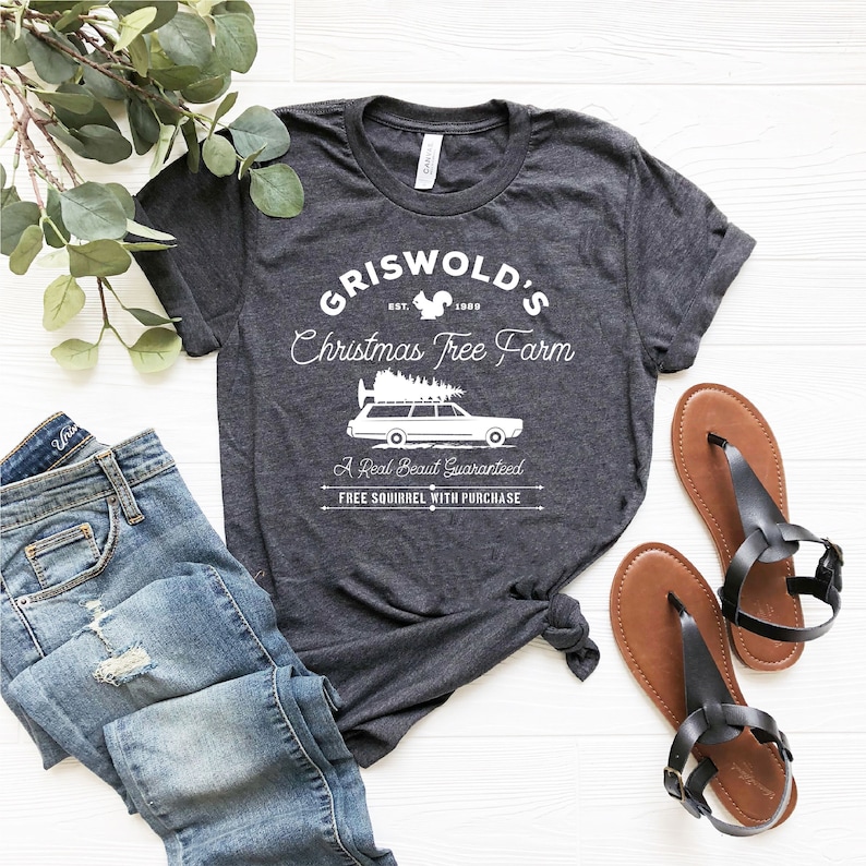 May include: A dark gray t-shirt with a white graphic design that says "Griswold's Christmas Tree Farm" with a squirrel and a station wagon with a Christmas tree on top. The text also says "Est. 1900", "A Real Beaut Guaranteed", and "Free Squirrel with Purchase".
