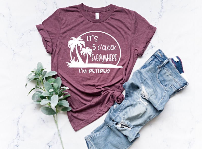 May include: A maroon t-shirt with a white graphic that says "It's 5 o'clock everywhere I'm retired" with palm trees and a sunset.