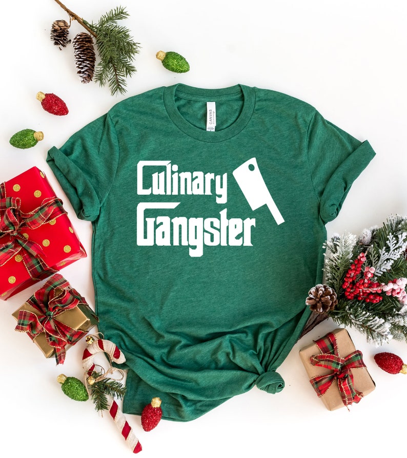 May include: Green t-shirt with white text that reads "Culinary Gangster" and a white silhouette of a butcher knife.