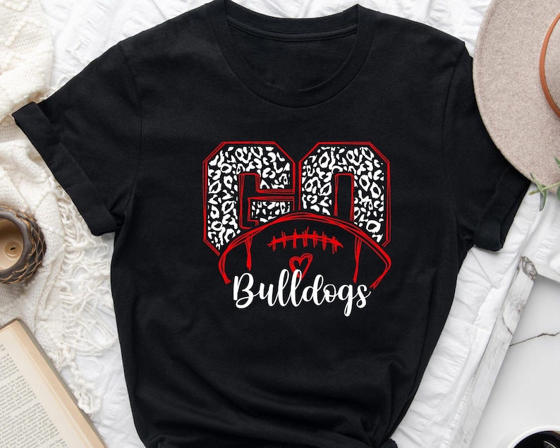 May include: Black t-shirt with a red and white leopard print design of the number 60 and a football with a red heart. The text "Bulldogs" is below the football.