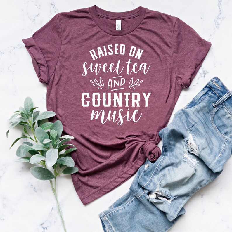 May include: A maroon t-shirt with the text "Raised on sweet tea and country music" in white lettering.