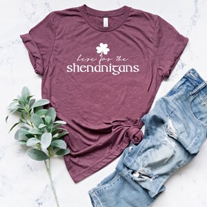 May include: A maroon t-shirt with a white shamrock and the text "here for the shenanigans".