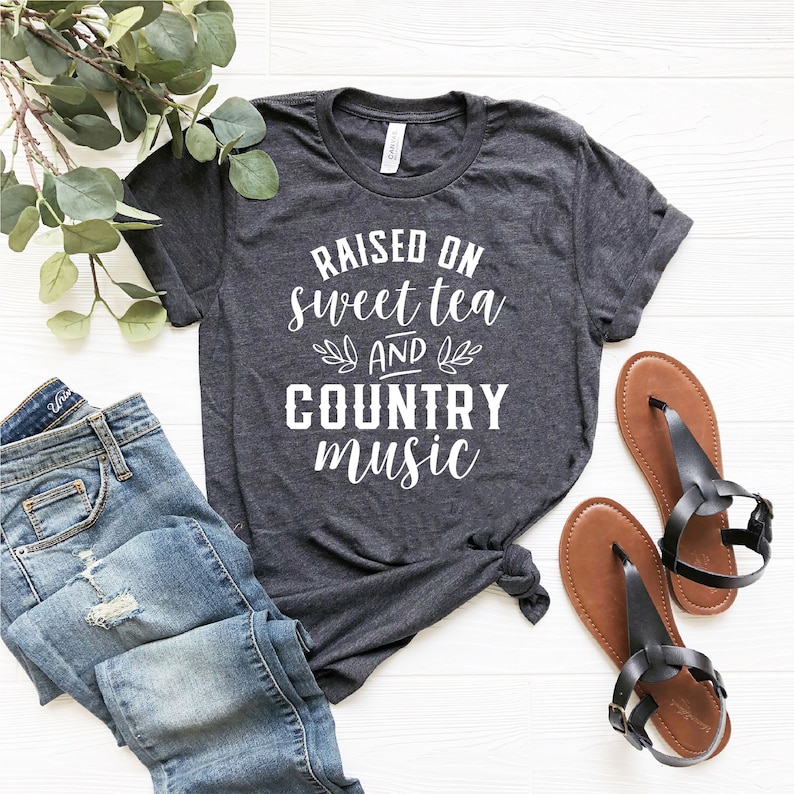 May include: A dark grey t-shirt with the text "Raised on sweet tea and country music" printed in white.