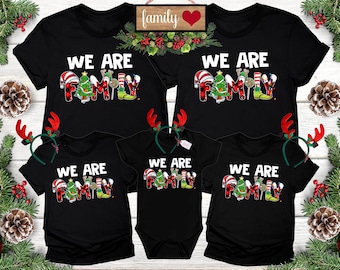 May include: Black family Christmas t-shirts with the text "WE ARE FAMILY" in white. The word "FAMILY" is designed with festive holiday elements. Includes a baby onesie and reindeer antlers.
