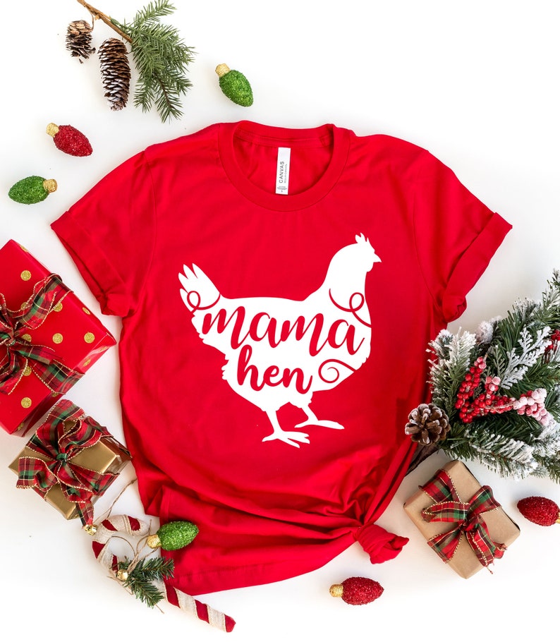 May include: Red t-shirt with a white silhouette of a chicken and the text "mama hen" on it. The shirt is laid out on a white surface with Christmas decorations around it.