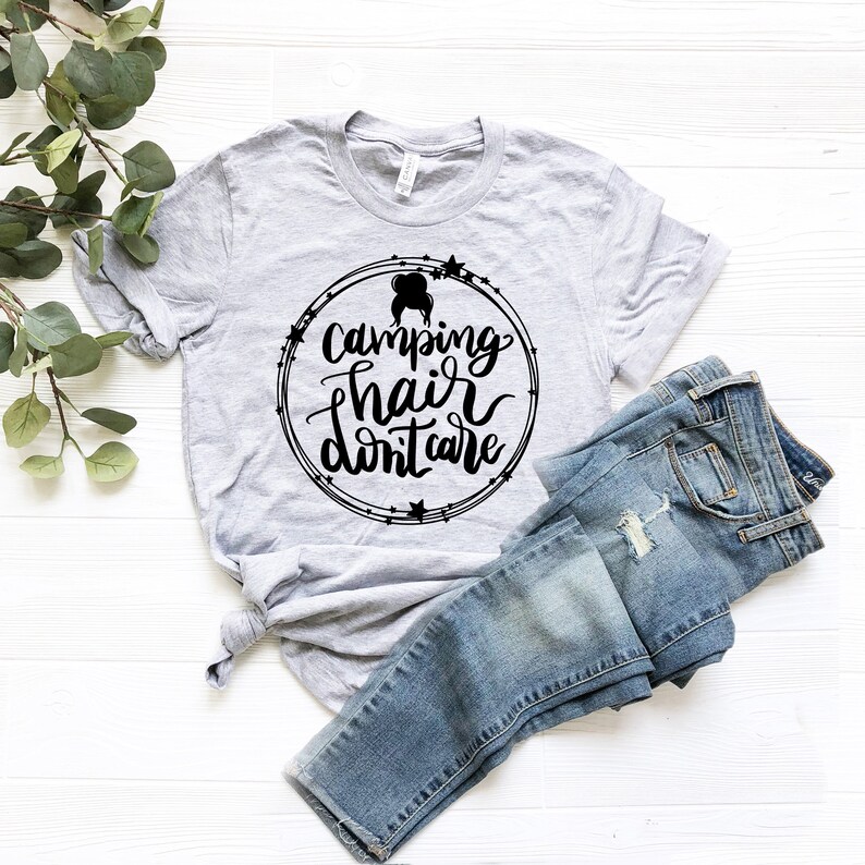 May include: A gray t-shirt with a black circle design that says "Camping hair don't care" with a silhouette of a woman with messy hair inside the circle.
