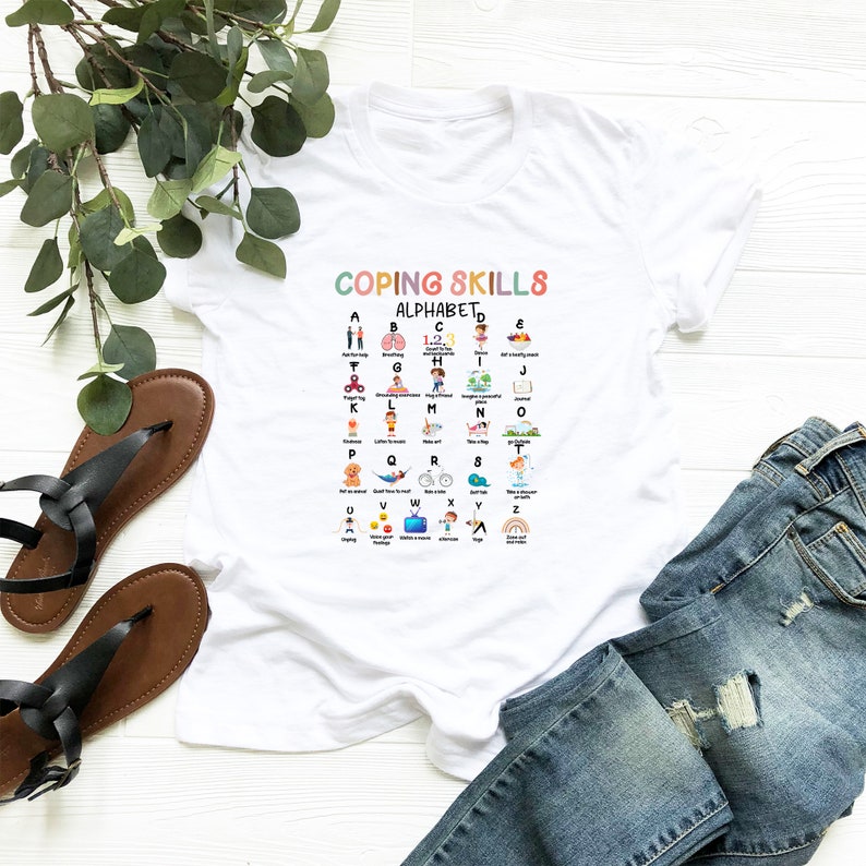May include: White t-shirt with a colorful alphabet chart listing coping skills for each letter. The chart is titled "Coping Skills Alphabet".