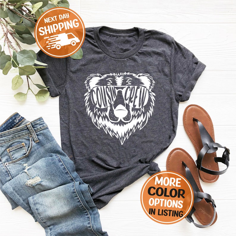 May include: Grey t-shirt with a white graphic of a bear wearing sunglasses with the text "Cousin Crew" inside the sunglasses.