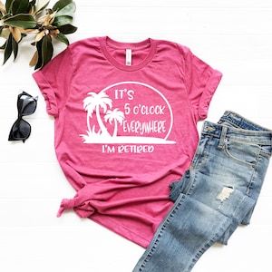 May include: Pink t-shirt with a white graphic that says "It's 5 o'clock everywhere I'm retired" with palm trees and a sunset.