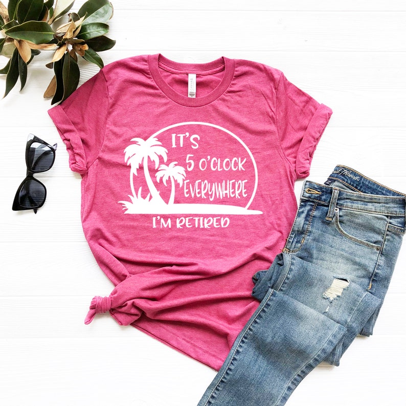 May include: Pink t-shirt with a white graphic that says "It's 5 o'clock everywhere I'm retired" with palm trees and a sunset.