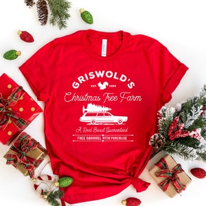 May include: Red t-shirt with a white graphic design that says "Griswold's Christmas Tree Farm" with a squirrel, the year 1989, and a cartoon car with a Christmas tree on top. The text below the graphic says "A Real Beaut Guaranteed" and "FREE SQUIRREL WITH PURCHASE."