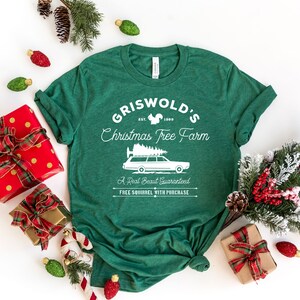 May include: Green t-shirt with a white graphic design that says "Griswold's Christmas Tree Farm" with a squirrel, a Christmas tree, and a station wagon with a Christmas tree on top. The text also says "Est. 1989", "A Real Beaut Guaranteed", and "Free Squirrel With Purchase".