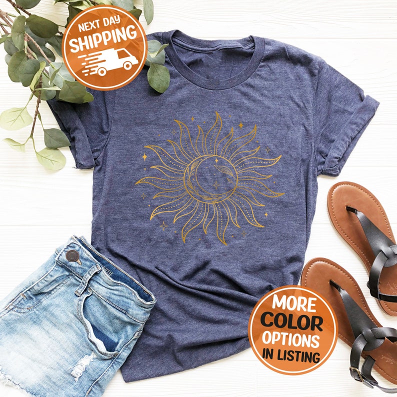 May include: A navy blue t-shirt with a gold sun and moon design. The sun has rays and the moon is crescent shaped. There are small stars around the sun and moon.