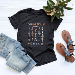 May include: Black t-shirt with a colorful graphic of the alphabet with coping skills for each letter. The graphic says "Coping Skills Alphabet".