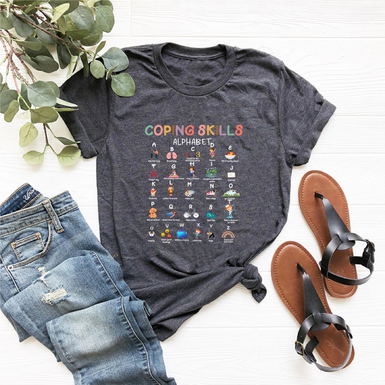 May include: A dark grey t-shirt with a colorful graphic that says "Coping Skills Alphabet" and features a list of coping skills for each letter of the alphabet.