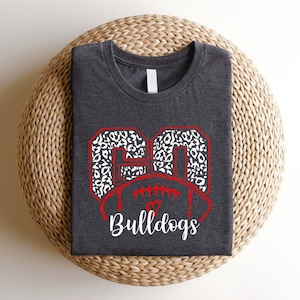 May include: A dark gray t-shirt with a white and black leopard print football design and the text "Bulldogs" in red.