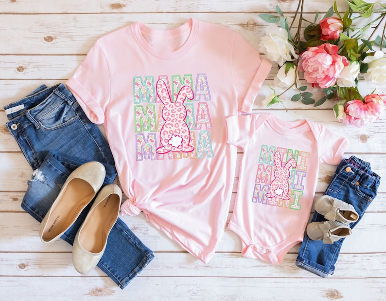 以下が含まれることがあります： ピンクのTシャツとボディースーツに、カラフルな花柄とヒョウ柄のウサギがプリントされています。Tシャツには「ママ」と、ボディースーツには「ミニミー」と書いてあります。