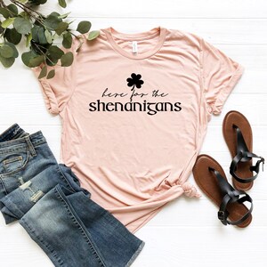 May include: A pink t-shirt with a black shamrock and the text "here for the shenanigans".