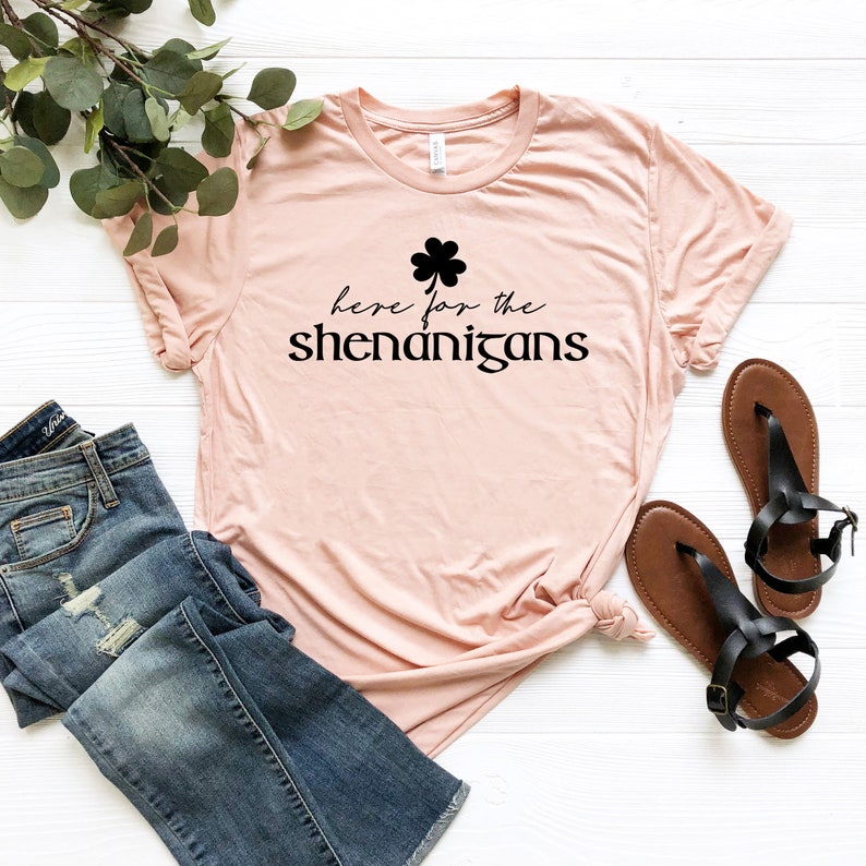 May include: A pink t-shirt with a black shamrock and the text "here for the shenanigans".