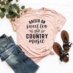 May include: A pink t-shirt with the text "RAISED ON sweet tea AND COUNTRY music" printed in black.