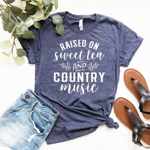 May include: A navy blue t-shirt with white text that reads "Raised on sweet tea and country music".