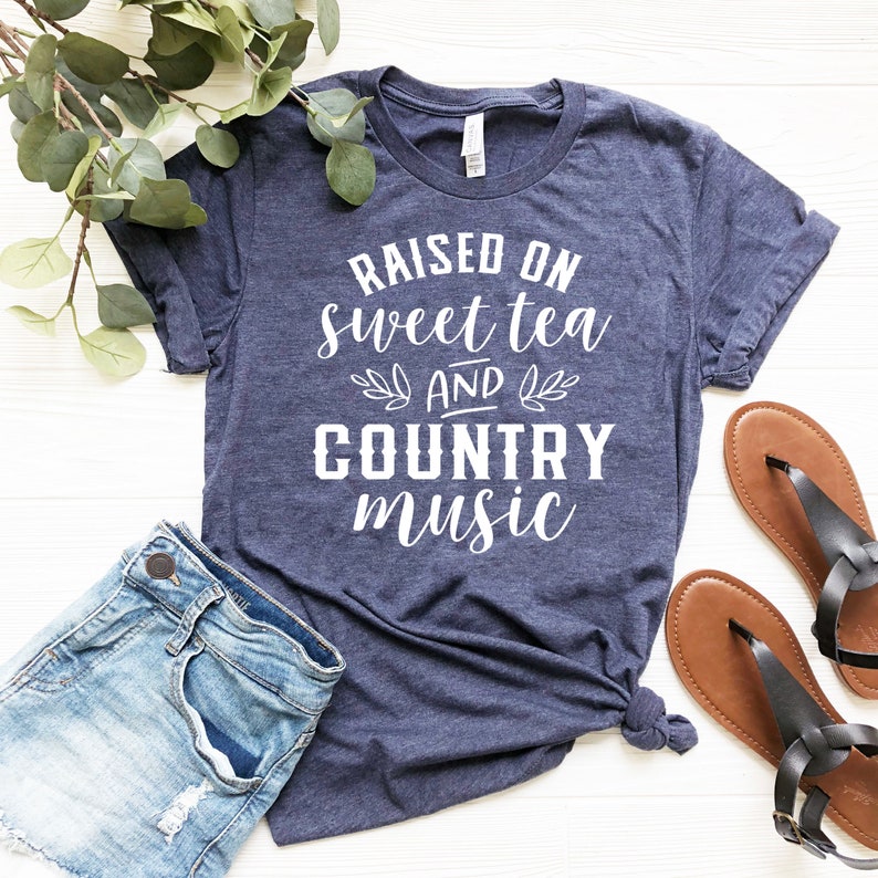May include: A navy blue t-shirt with white text that reads "Raised on sweet tea and country music".