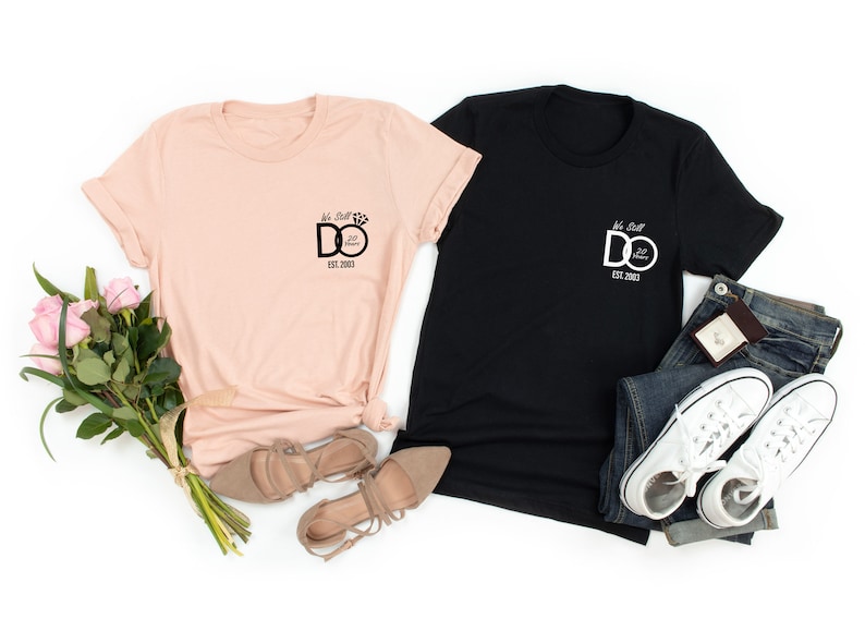May include: Two t-shirts with a graphic of a ring with the text "We Still Do" and "Est. 2023". The t-shirts are in pink and black.