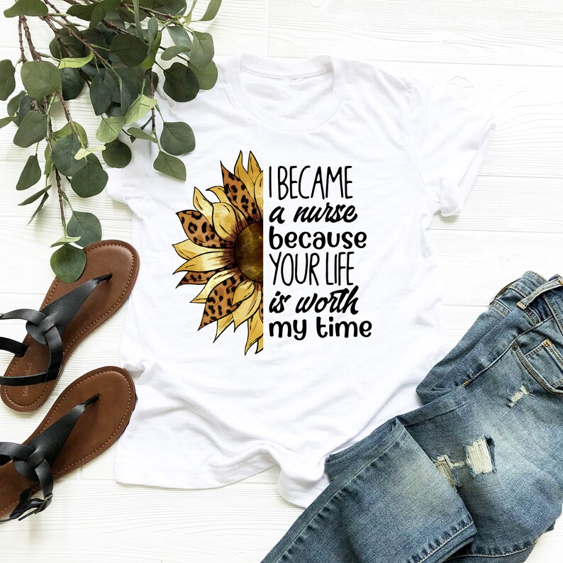 Op de afbeelding: Wit T-shirt met een zonnebloemgrafiek en de tekst "Ik ben verpleegster geworden omdat je leven mijn tijd waard is".