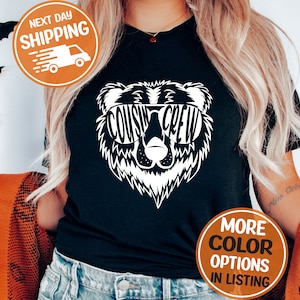 May include: Black t-shirt featuring a white bear graphic wearing sunglasses. The sunglasses spell out "COUSIN CREW".