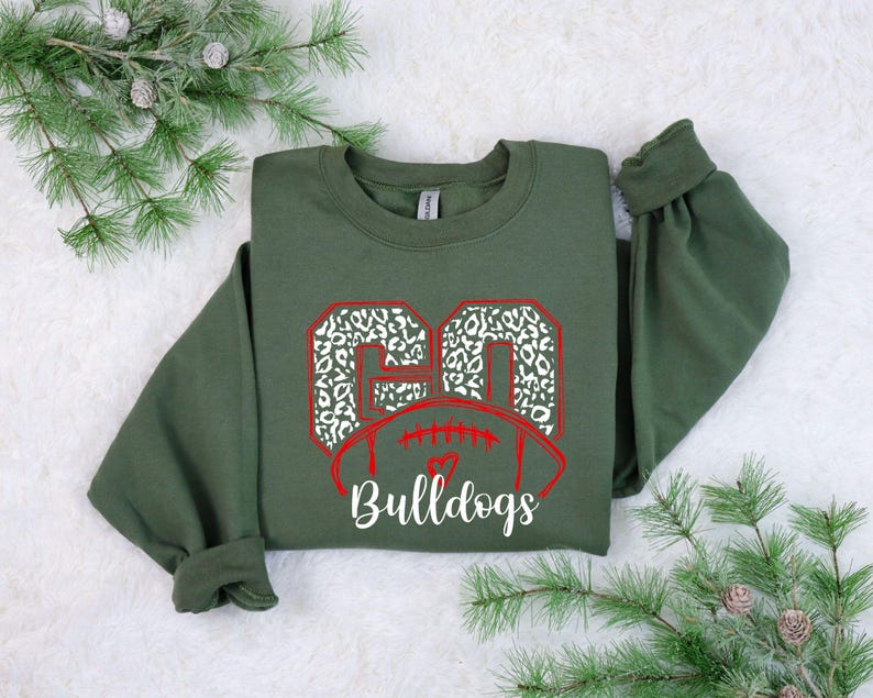 May include: Green sweatshirt with a red and white football design. The football has the number 60 in white with a leopard print pattern. The text "Bulldogs" is below the football.
