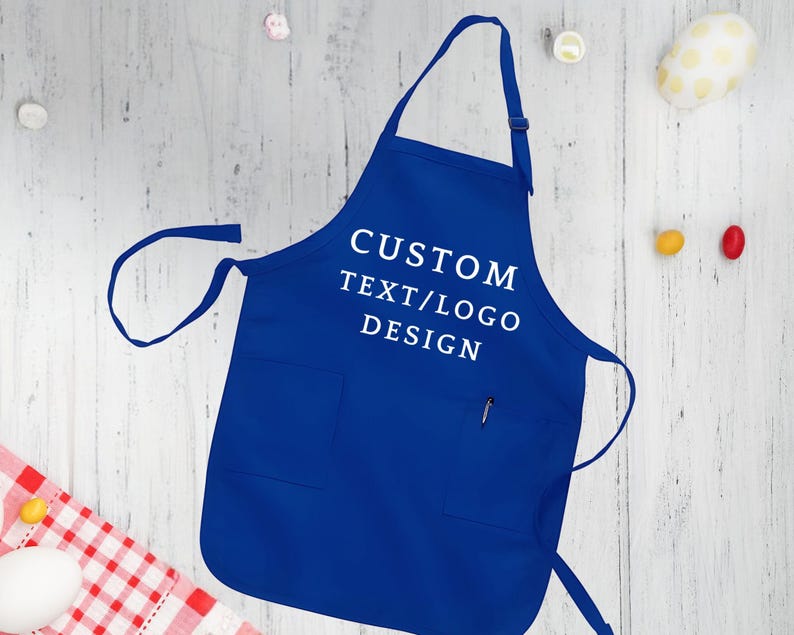 May include: A royal blue apron with a large pocket and adjustable straps. The apron has white text that reads "CUSTOM TEXT/LOGO DESIGN".