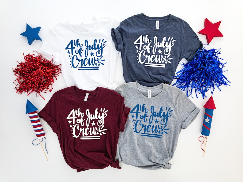 May include: Four t-shirts in white, navy, burgundy, and gray, each with the text "4th of July Crew" in a script font. Decorative stars and fireworks elements surround the text. Patriotic theme.