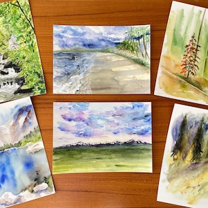 May include: A collection of five watercolor paintings depicting various landscapes. Scenes include a waterfall, a beach with palm trees, a forest with a single tree, a mountain lake, and a field with mountains under a cloudy sky.