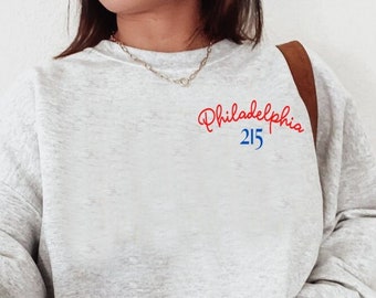 May include: A gray sweatshirt with a red and blue embroidered design that says "Philadelphia 215" on the left chest.