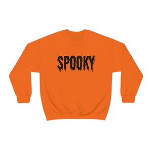 May include: Orange sweatshirt with the word "SPOOKY" in black, dripping font. The crew neck sweatshirt is a solid orange color, perfect for Halloween or spooky season.