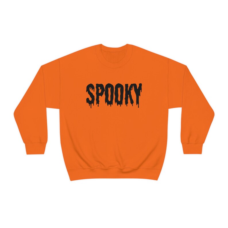 May include: Orange sweatshirt with the word "SPOOKY" in black, dripping font. The crew neck sweatshirt is a solid orange color, perfect for Halloween or spooky season.