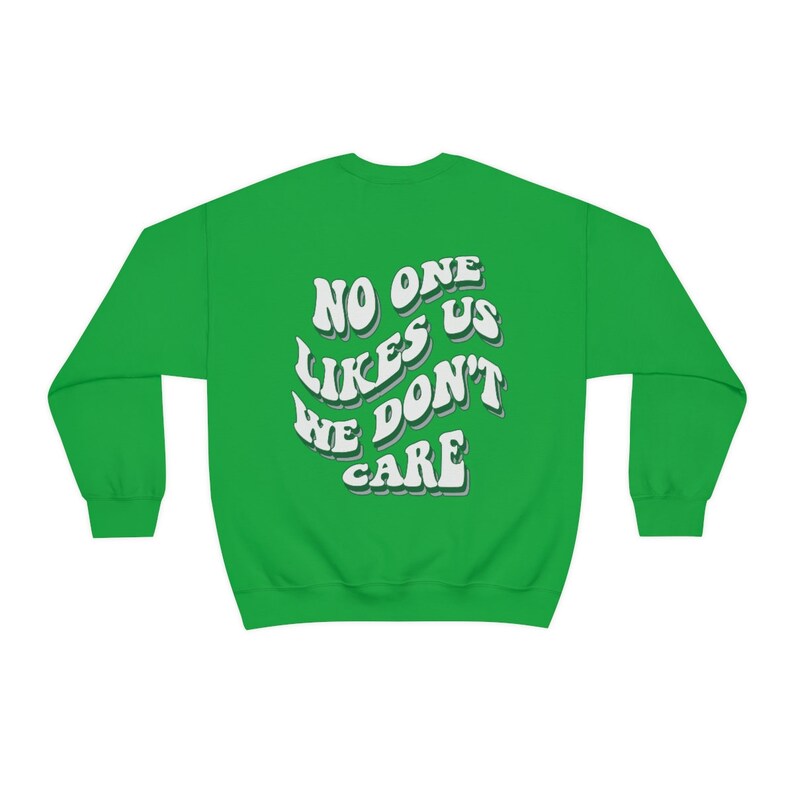 Może przedstawiać: Zielony sweter z białym napisem "No one likes us we don't care" w retro czcionce.