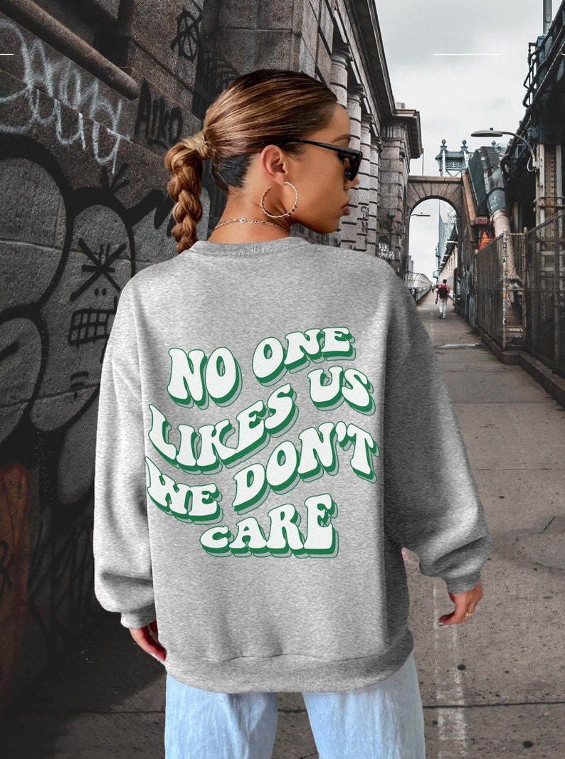 Może przedstawiać: Szara bluza z zielonym nadrukiem graficznym, na kt&oacute;rym widnieje napis "No one likes us we don't care".